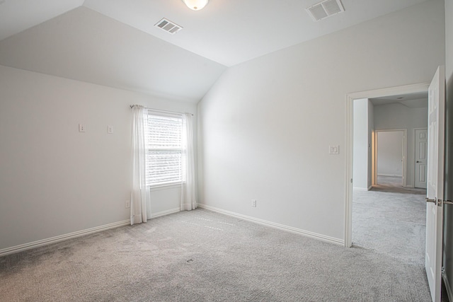 spare room featuring light carpet, lofted ceiling, visible vents, and baseboards