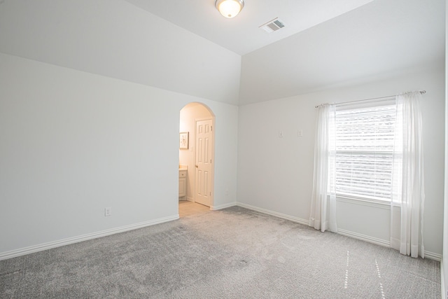 spare room featuring light carpet, arched walkways, baseboards, visible vents, and lofted ceiling
