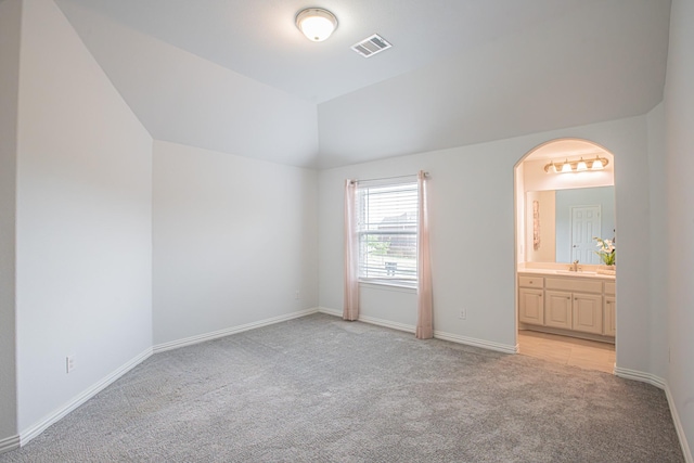 unfurnished bedroom with lofted ceiling, visible vents, arched walkways, baseboards, and light colored carpet