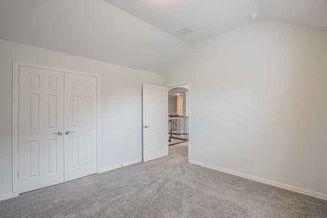 unfurnished bedroom with carpet flooring, arched walkways, vaulted ceiling, visible vents, and a closet