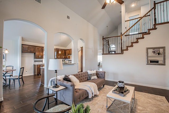 living room featuring dark wood finished floors, visible vents, a ceiling fan, arched walkways, and high vaulted ceiling