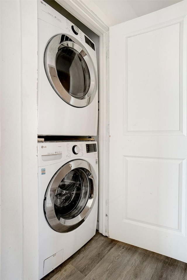 laundry room featuring stacked washer / drying machine, wood finished floors, and laundry area
