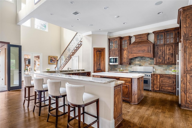 6511 Mimosa Ln, Dallas, TX 75230 - kitchen with a large island with sink, stainless steel appliances, premium range hood, dark wood finished floors, and crown molding