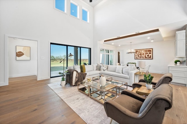 living area featuring baseboards, an inviting chandelier, a towering ceiling, and light wood-style floors