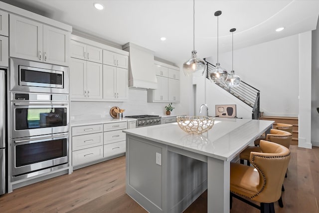 kitchen with a kitchen breakfast bar, a center island with sink, custom exhaust hood, recessed lighting, and light wood-style floors