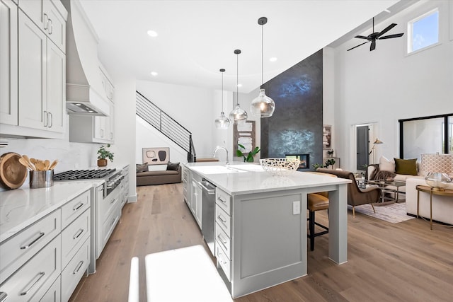 kitchen featuring light wood finished floors, open floor plan, custom exhaust hood, a large fireplace, and ceiling fan