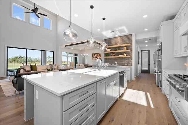 kitchen with a ceiling fan, open shelves, a sink, an island with sink, and stainless steel appliances