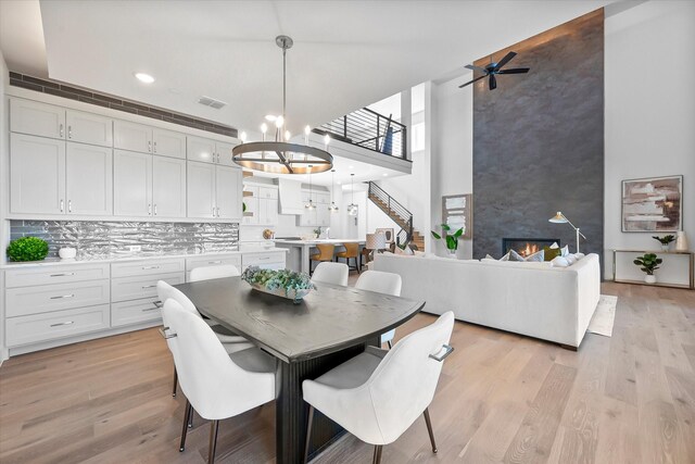 dining area featuring ceiling fan with notable chandelier, a towering ceiling, light wood finished floors, a fireplace, and visible vents