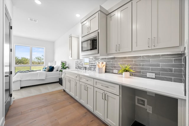 kitchen with a sink, stainless steel microwave, light wood-style floors, decorative backsplash, and open floor plan