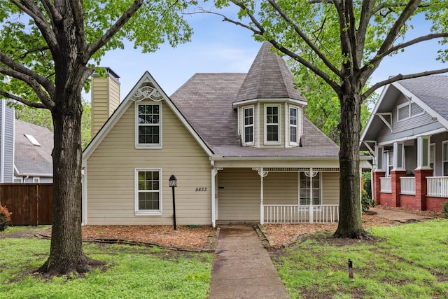 victorian-style house featuring a porch, a chimney, fence, and a front yard