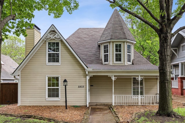 victorian house featuring fence, a chimney, and covered porch