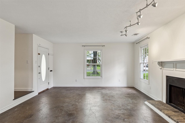 unfurnished living room with a textured ceiling, a fireplace with raised hearth, concrete flooring, track lighting, and visible vents