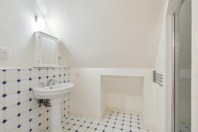 bathroom with vaulted ceiling, tile walls, tile patterned floors, and tiled shower