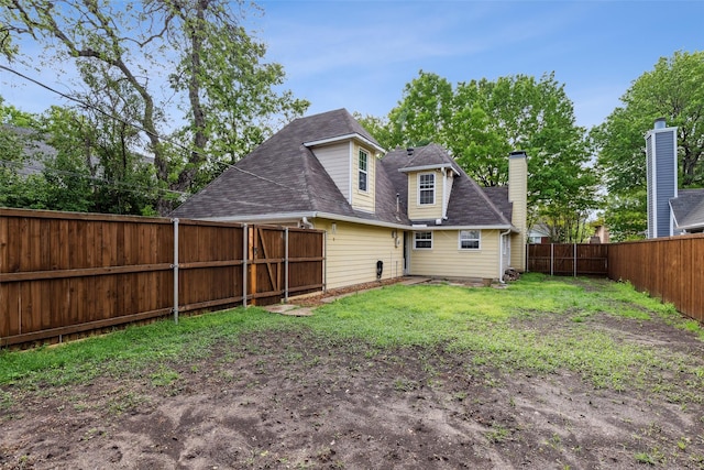 back of house featuring a fenced backyard, roof with shingles, and a lawn