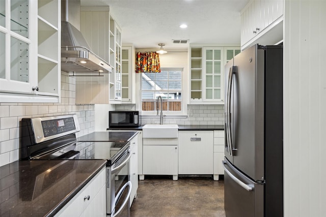 kitchen featuring a sink, backsplash, concrete flooring, wall chimney range hood, and appliances with stainless steel finishes
