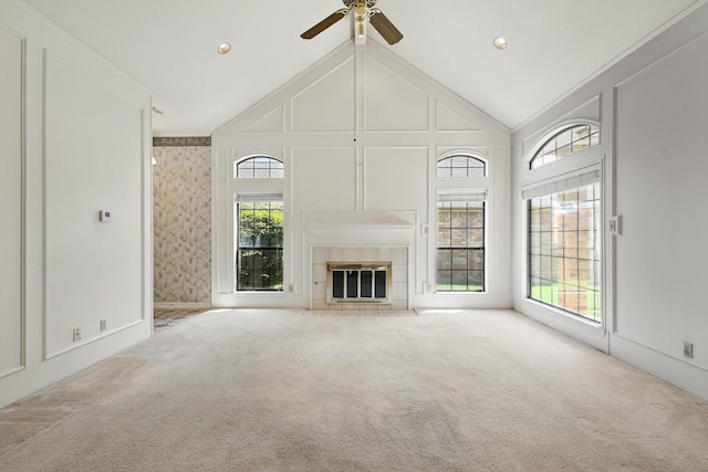 unfurnished living room with a tiled fireplace, carpet flooring, high vaulted ceiling, and ceiling fan