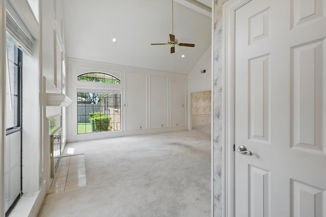 carpeted spare room with a ceiling fan, high vaulted ceiling, and a decorative wall