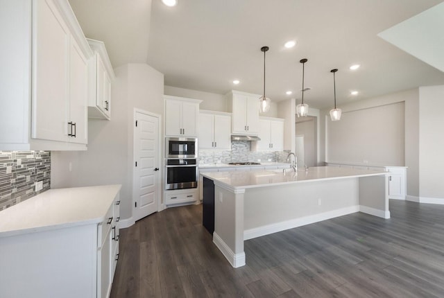 kitchen featuring white cabinets, stainless steel appliances, a large island with sink, and tasteful backsplash