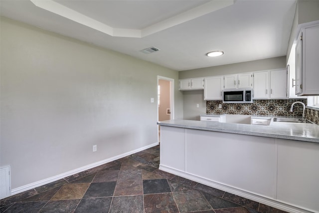 kitchen with a sink, stainless steel microwave, baseboards, white cabinetry, and stone finish floor