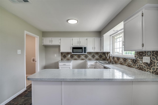 kitchen featuring white cabinets, a sink, stainless steel microwave, a peninsula, and tasteful backsplash