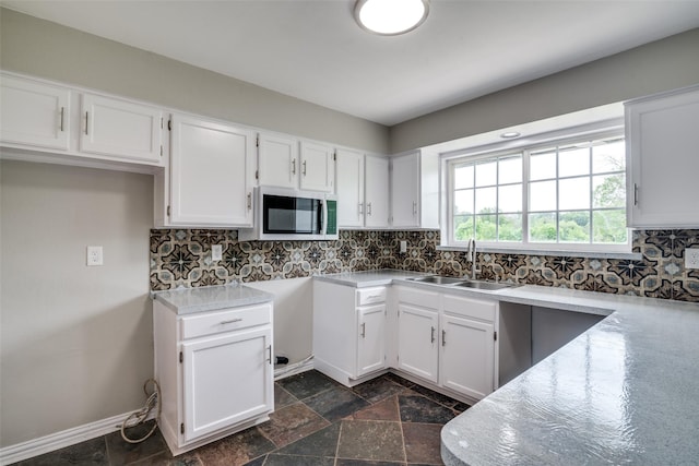 kitchen with a sink, white cabinets, decorative backsplash, stone tile flooring, and stainless steel microwave