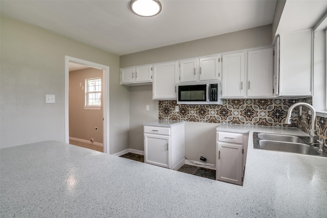 kitchen featuring light countertops, a sink, stainless steel microwave, tasteful backsplash, and white cabinetry