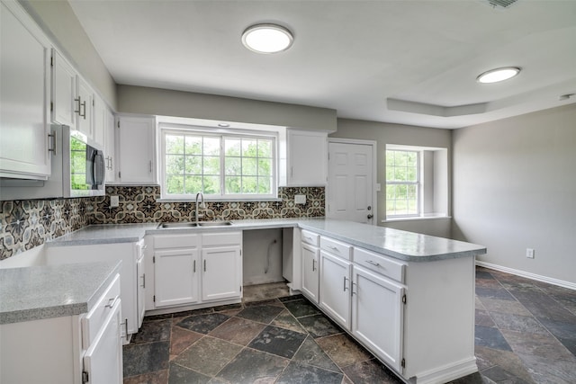 kitchen with white cabinets, backsplash, a sink, stone tile flooring, and a peninsula