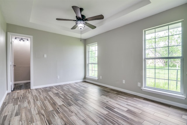 unfurnished room with a tray ceiling, wood finished floors, and baseboards
