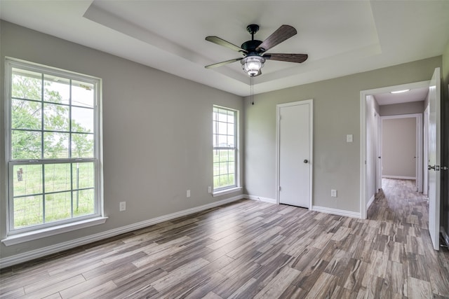 unfurnished bedroom with a raised ceiling, wood finished floors, baseboards, and ceiling fan