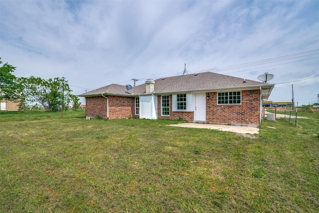 back of house featuring a yard, brick siding, a patio area, and a shingled roof