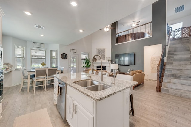 kitchen with visible vents, stainless steel dishwasher, light wood-type flooring, a sink, and open floor plan