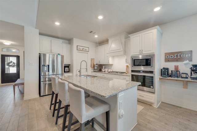kitchen with appliances with stainless steel finishes, a sink, white cabinetry, custom range hood, and visible vents