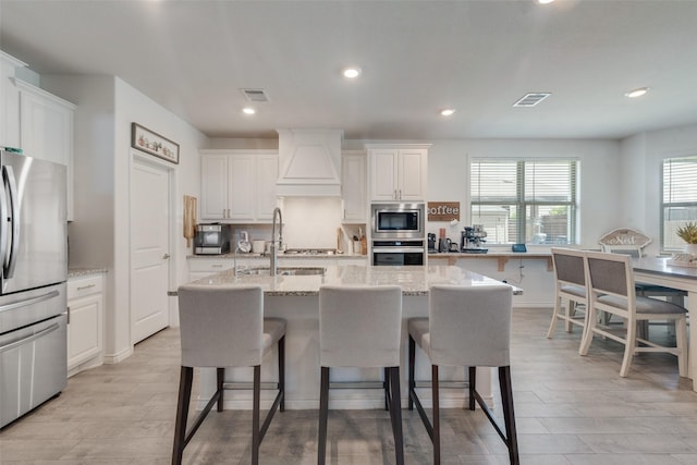 kitchen featuring a breakfast bar area, premium range hood, white cabinets, a sink, and stainless steel appliances