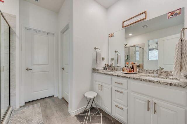full bath with wood finished floors, double vanity, a sink, and a stall shower