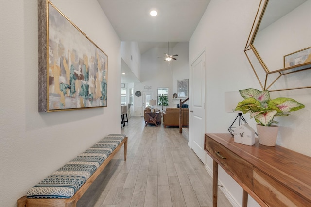 hall featuring light wood-type flooring, recessed lighting, and a towering ceiling