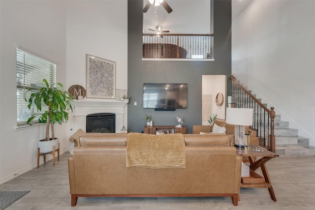 living area featuring a high ceiling, a glass covered fireplace, a ceiling fan, a wealth of natural light, and stairway