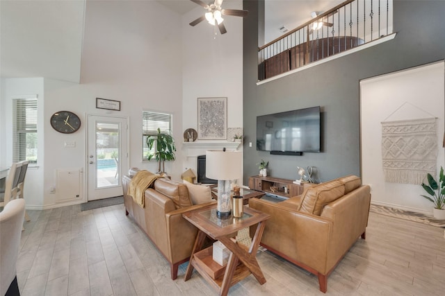 living room featuring a ceiling fan, light wood-style flooring, and a towering ceiling