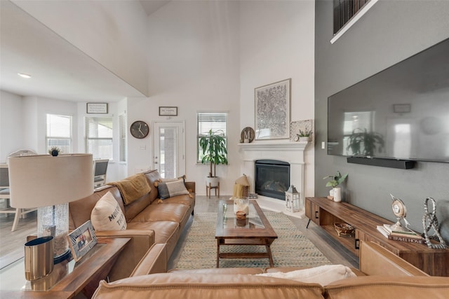 living room featuring a high ceiling, a glass covered fireplace, and wood finished floors