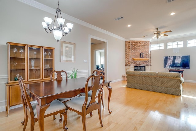 11632 Virginia Way Ct, Fort Worth, TX 76008 - dining room with light wood-type flooring, visible vents, ceiling fan with notable chandelier, a brick fireplace, and crown molding