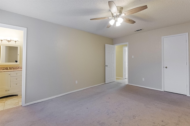 unfurnished bedroom with light carpet, a textured ceiling, ensuite bathroom, visible vents, and baseboards