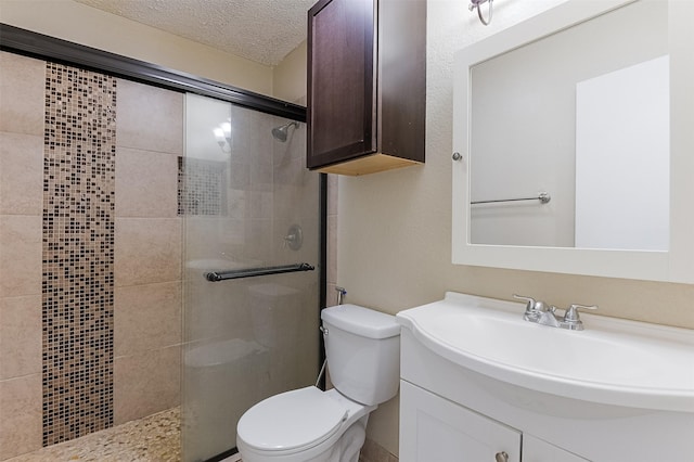 bathroom with toilet, vanity, a textured ceiling, and tiled shower
