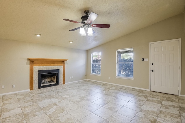 unfurnished living room featuring a textured ceiling, a tiled fireplace, vaulted ceiling, baseboards, and a ceiling fan