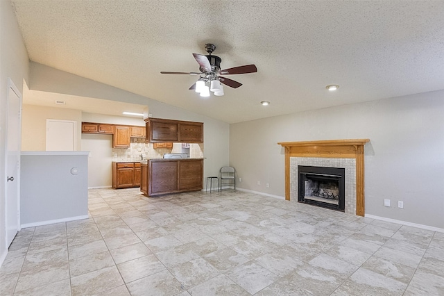 kitchen featuring lofted ceiling, backsplash, a fireplace, brown cabinetry, and ceiling fan
