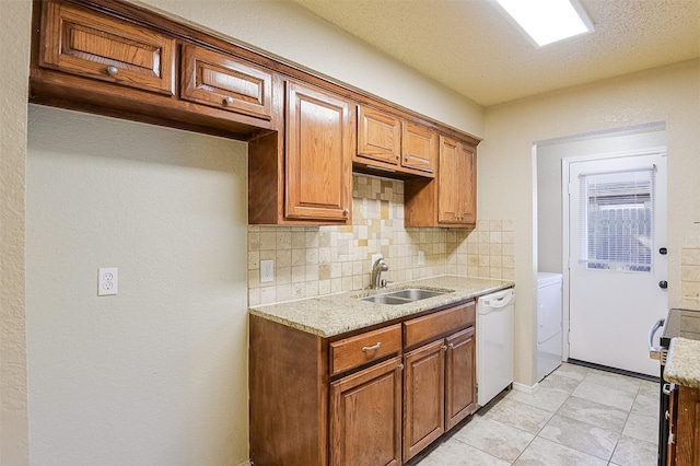 kitchen featuring brown cabinetry, a sink, white dishwasher, washer / dryer, and tasteful backsplash