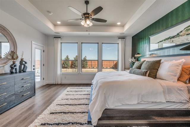 bedroom featuring recessed lighting, a tray ceiling, wood finished floors, baseboards, and access to outside