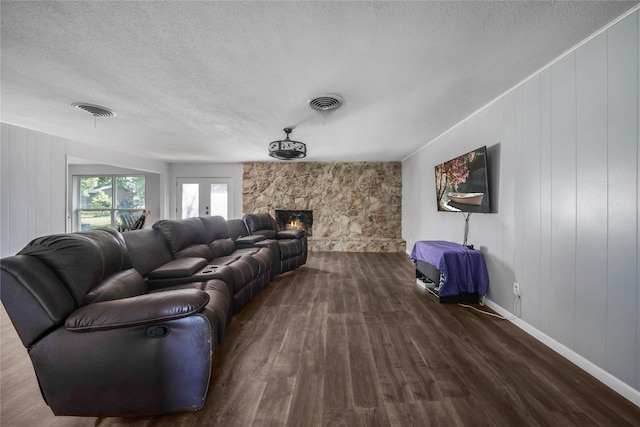 living room featuring a stone fireplace, visible vents, a textured ceiling, and dark wood-style flooring