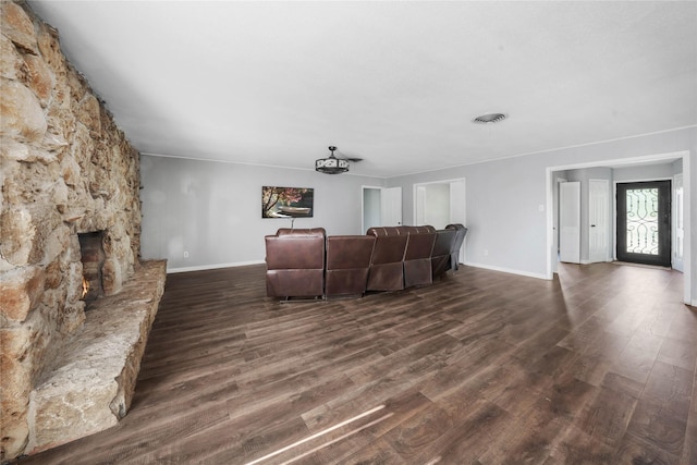 living room featuring dark wood-type flooring, visible vents, baseboards, and a fireplace
