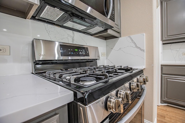 room details featuring tasteful backsplash, light stone countertops, gray cabinetry, light wood finished floors, and stainless steel appliances