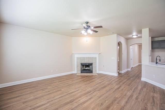 unfurnished living room with visible vents, a sink, ceiling fan, arched walkways, and light wood-style flooring