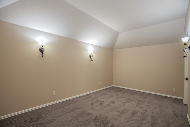 empty room with baseboards, vaulted ceiling, and dark carpet